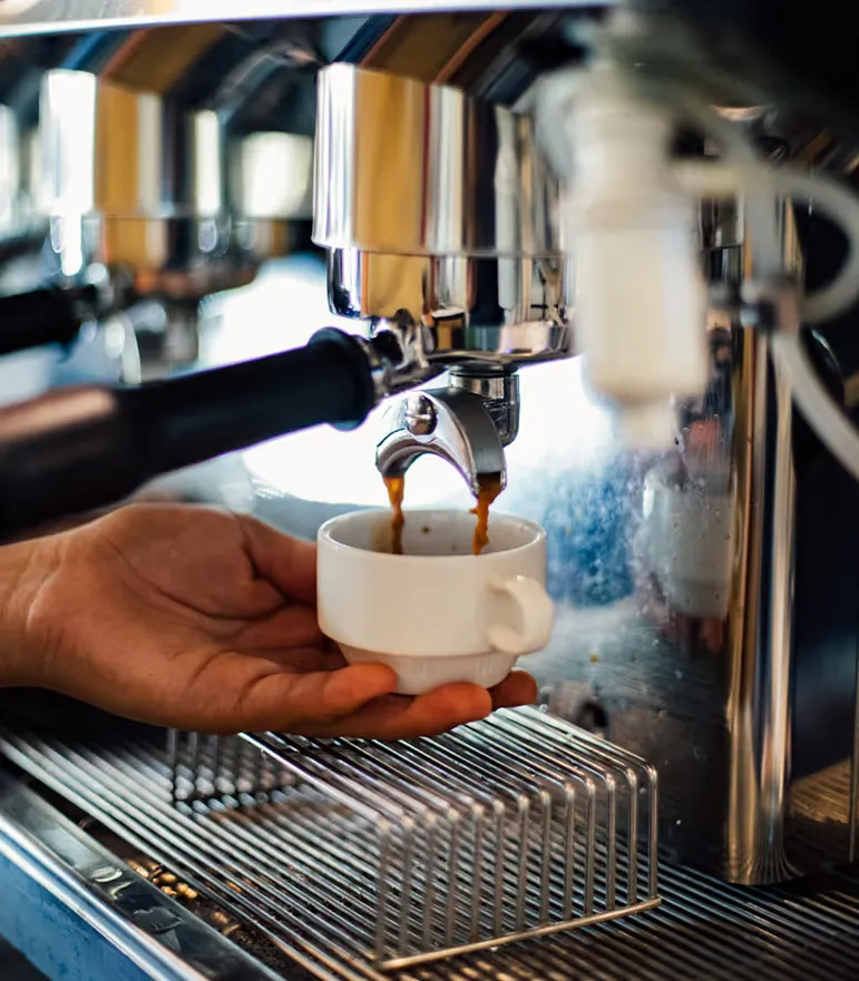Primer plano de un espresso cayendo en una taza blanca bajo la máquina de café.