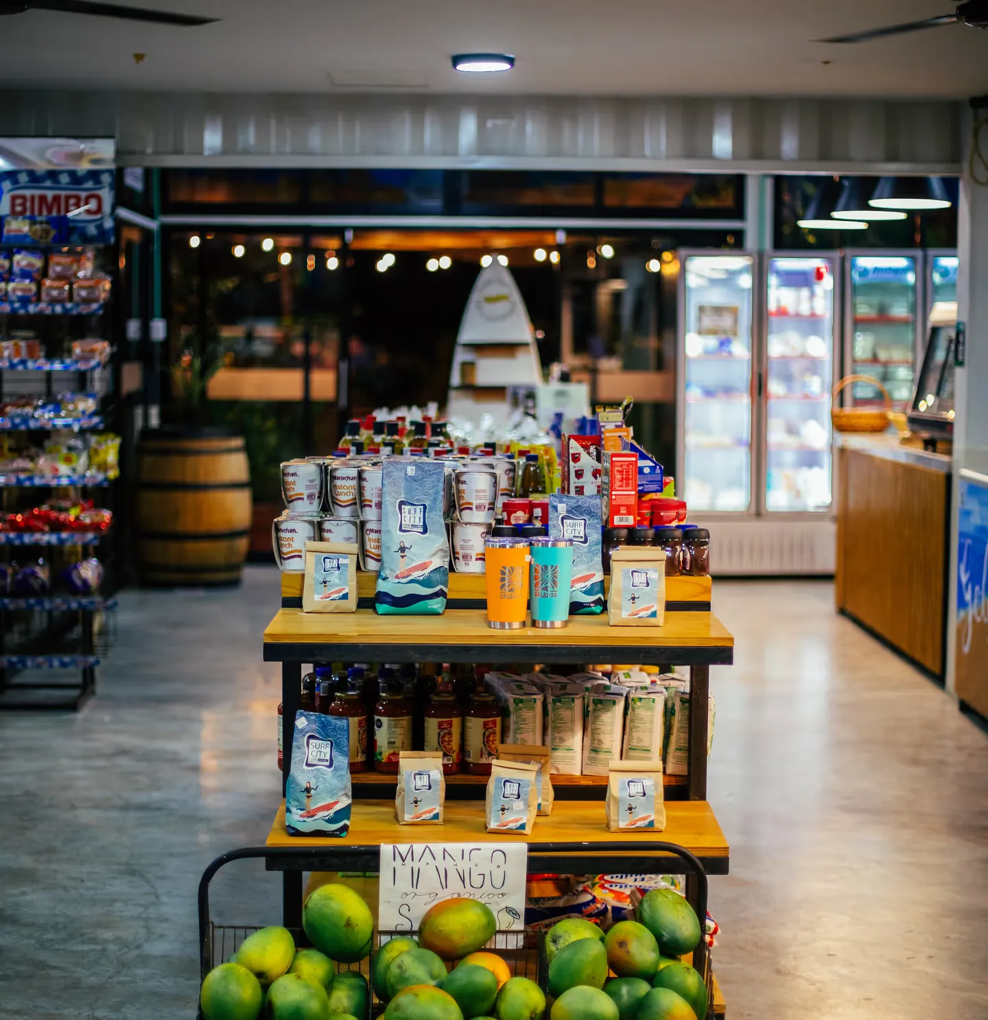 Interior de La Esquina con estantes, un exhibidor de productos locales y mangos frescos en una caja.