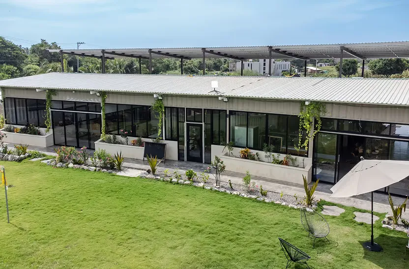 Fachada de Hacienda Plaza: el corredor techado de locales con puertas de cristal frente al jardín.