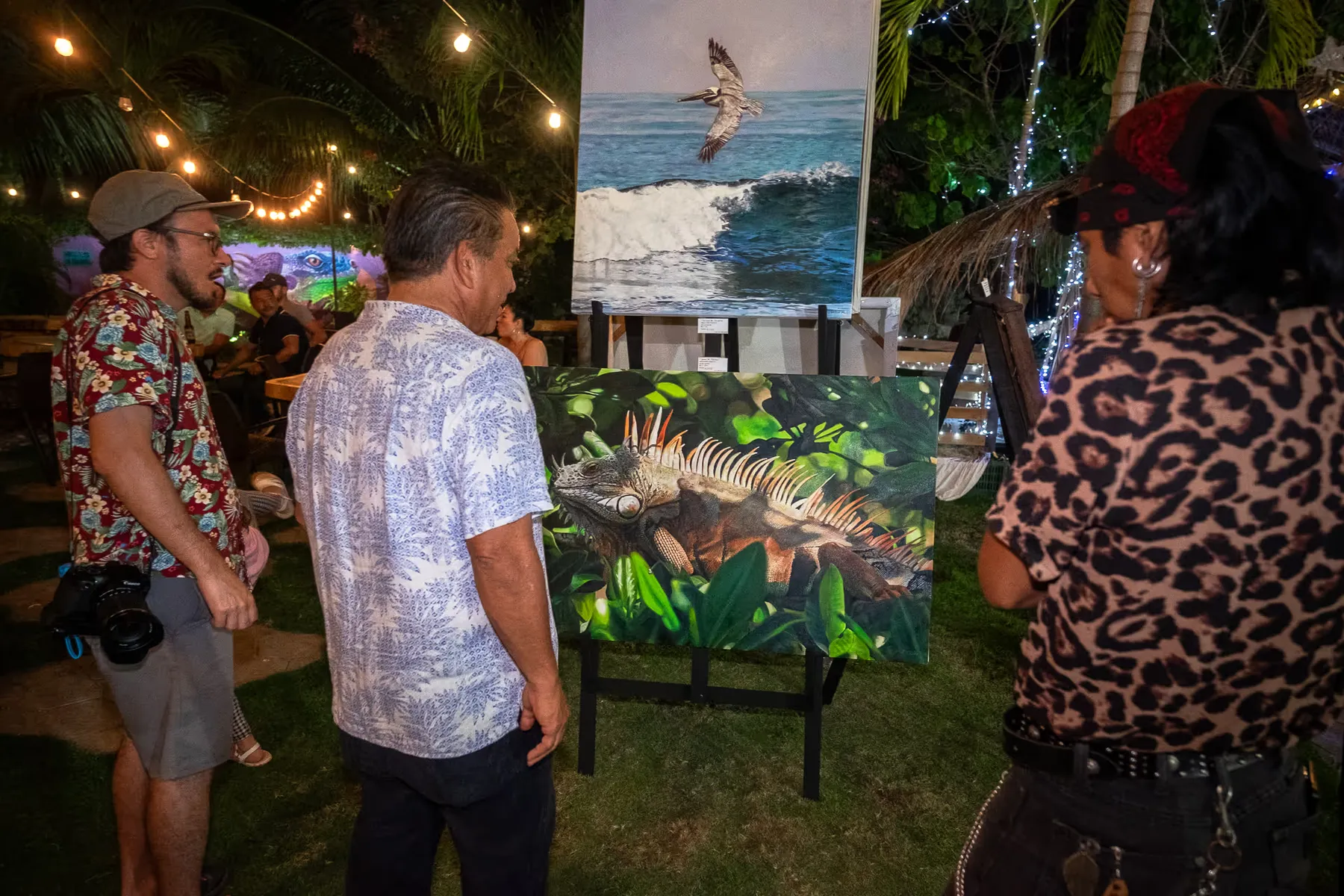 Noche en el jardín con impresiones de fotografía de surf sobre caballetes y luces colgadas entre los árboles.